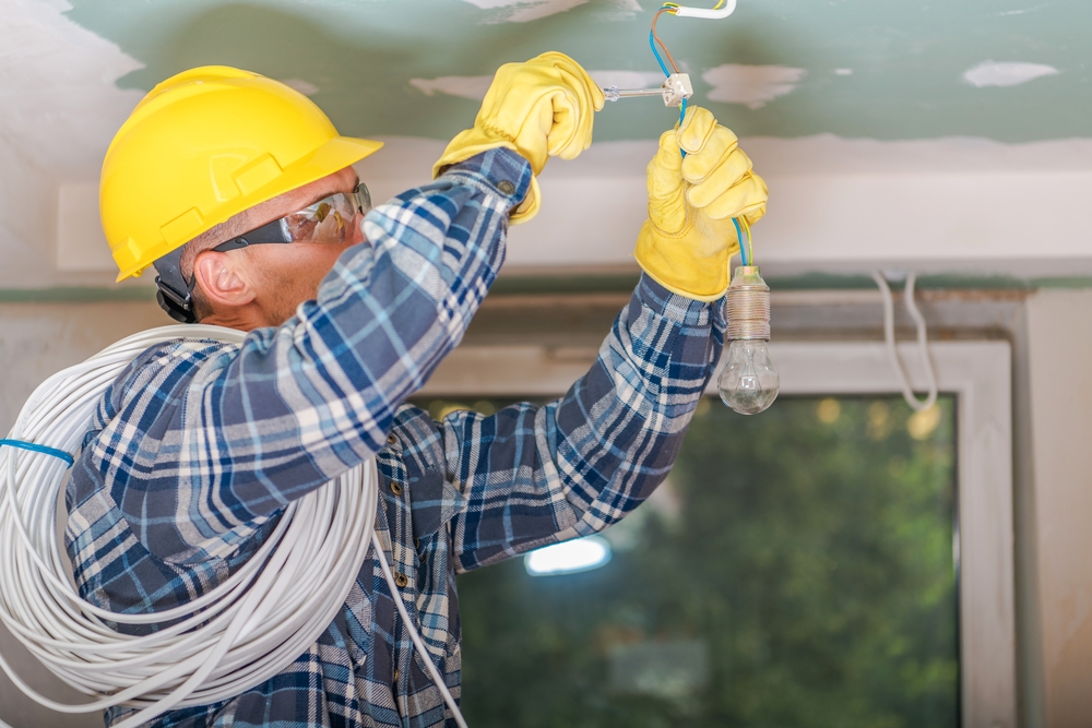 Caucasian Electrician in Yellow Safety Hard Hat at Work. Reinstallation of Residential Electrical System.